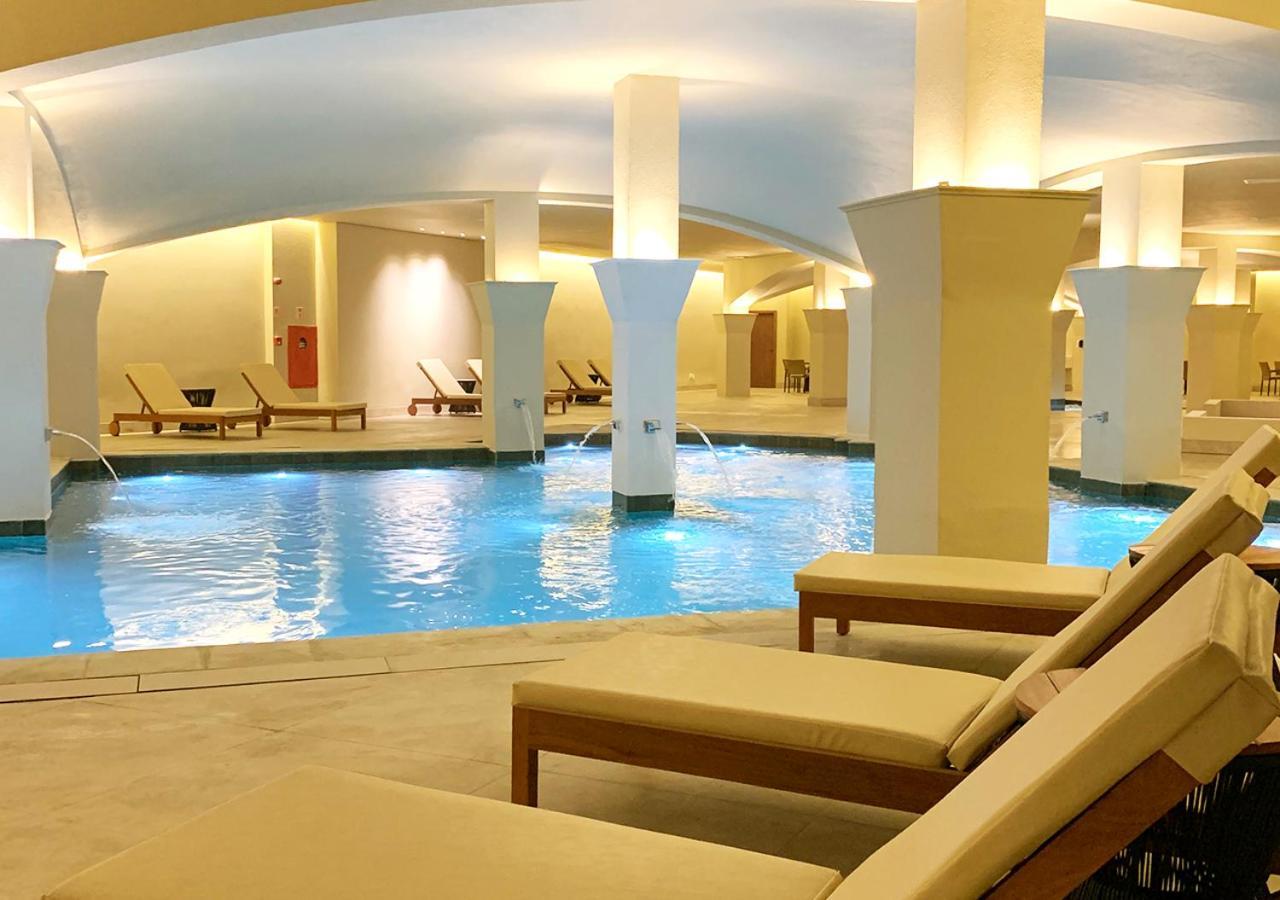 Buona Vitta Gramado Resort & Spa By Gramado Parks Buitenkant foto The photo shows an indoor spa or relaxation area with a tranquil atmosphere. There is a large swimming pool with clear blue water, illuminated by soft lighting. Surrounding the pool are several comfortable lounge chairs. The architecture features ele