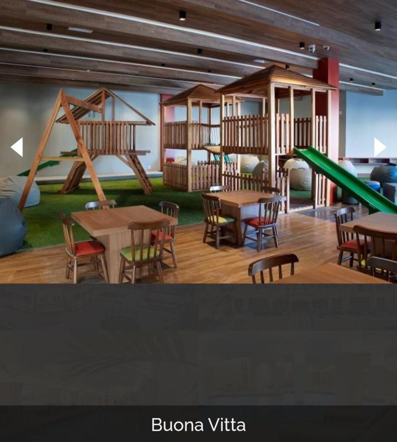 Buona Vitta Gramado Resort & Spa By Gramado Parks Buitenkant foto The photo shows a play area designed for children, featuring a wooden play structure with slides and climbing areas. In the foreground, there are several small wooden tables and chairs arranged for seating. The floor is covered with green turf, resem