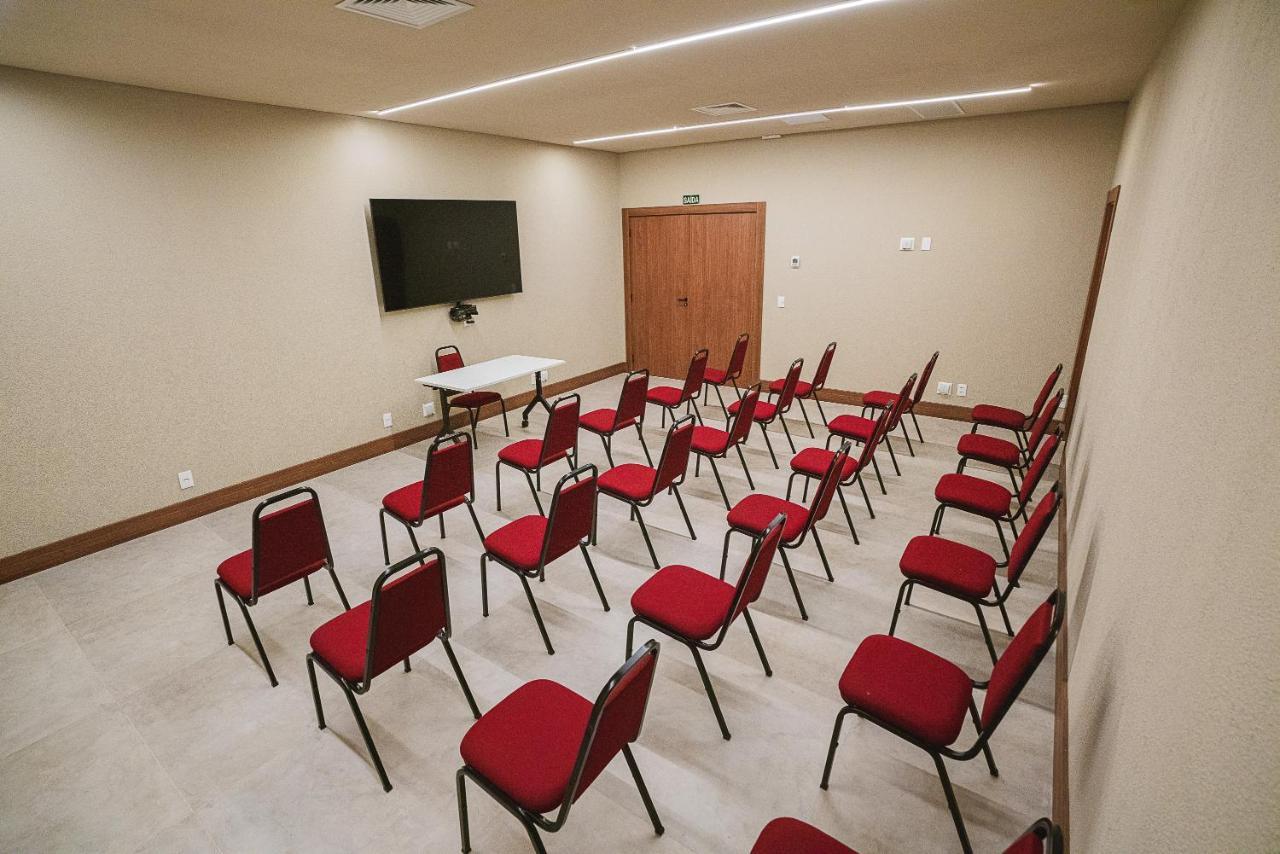 Buona Vitta Gramado Resort & Spa By Gramado Parks Buitenkant foto The photo shows a conference or meeting room with a simple and modern design. There are several rows of red chairs arranged in a semi-circle facing a white table at the front. On the wall opposite the chairs, there is a flat-screen television mounted