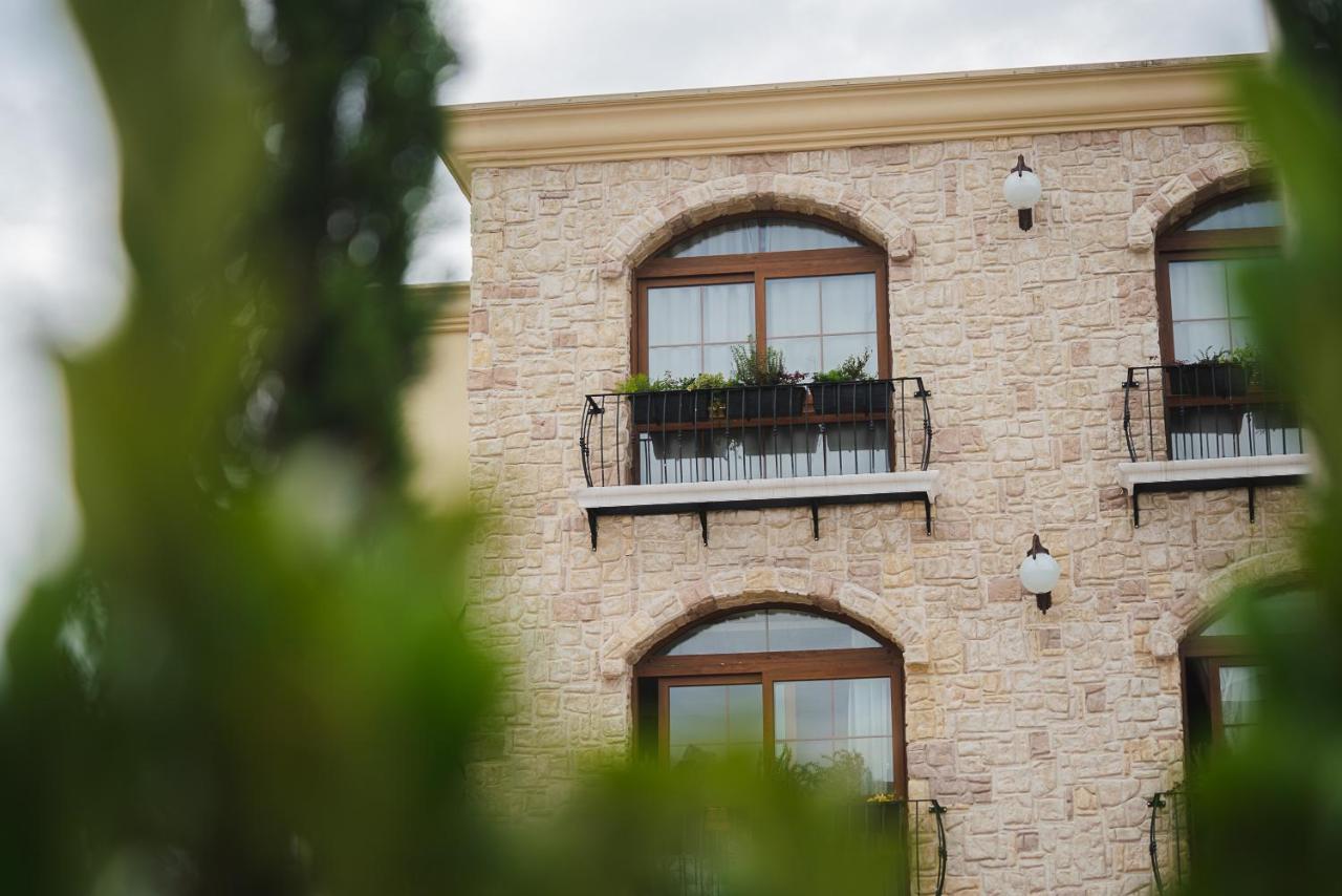 Buona Vitta Gramado Resort & Spa By Gramado Parks Buitenkant foto The photo depicts a stone building with a textured exterior. It features several windows with wooden frames. Each window has a small balcony adorned with decorative plants. There are also wall-mounted light fixtures flanking the windows. In the foreg