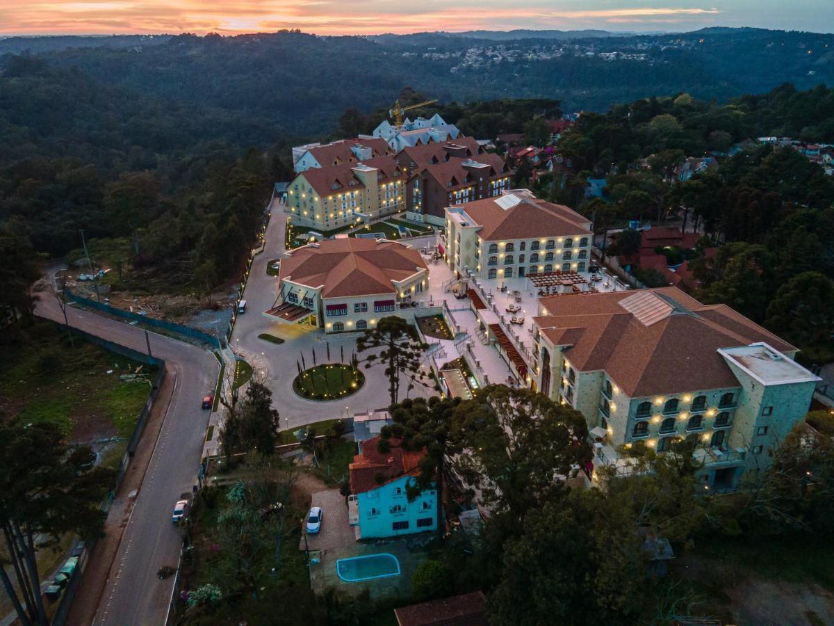 Buona Vitta Gramado Resort & Spa By Gramado Parks Buitenkant foto The photo shows an aerial view of a hotel complex set in a hilly, wooded area. The buildings feature a mix of architectural styles with several structures, including a central round pavilion. Surrounding the buildings are well-maintained gardens and 