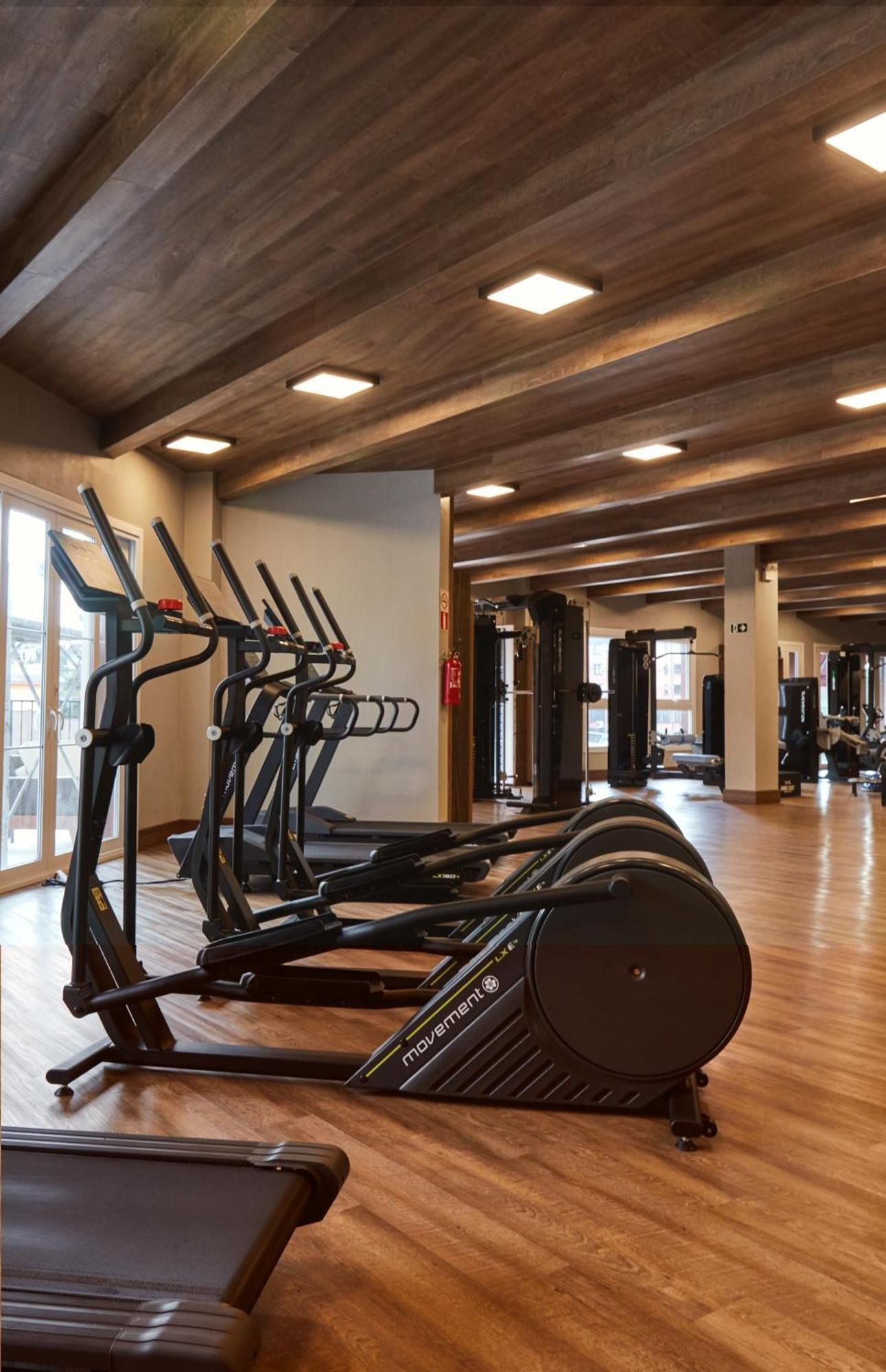 Buona Vitta Gramado Resort & Spa By Gramado Parks Buitenkant foto The photo shows a modern gym interior with wooden flooring and a ceiling with wooden beams. There are several exercise machines, including elliptical trainers and a treadmill, positioned in the foreground. In the background, there are additional work