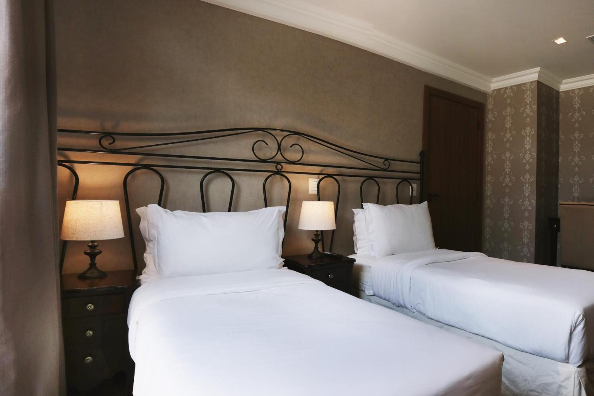 Buona Vitta Gramado Resort & Spa By Gramado Parks Buitenkant foto The photo shows a neatly arranged hotel room featuring two single beds with white bedding. The beds have decorative metal headboards, and there are bedside tables on either side with lamps. The room's walls have a subtle design, and there is a door v