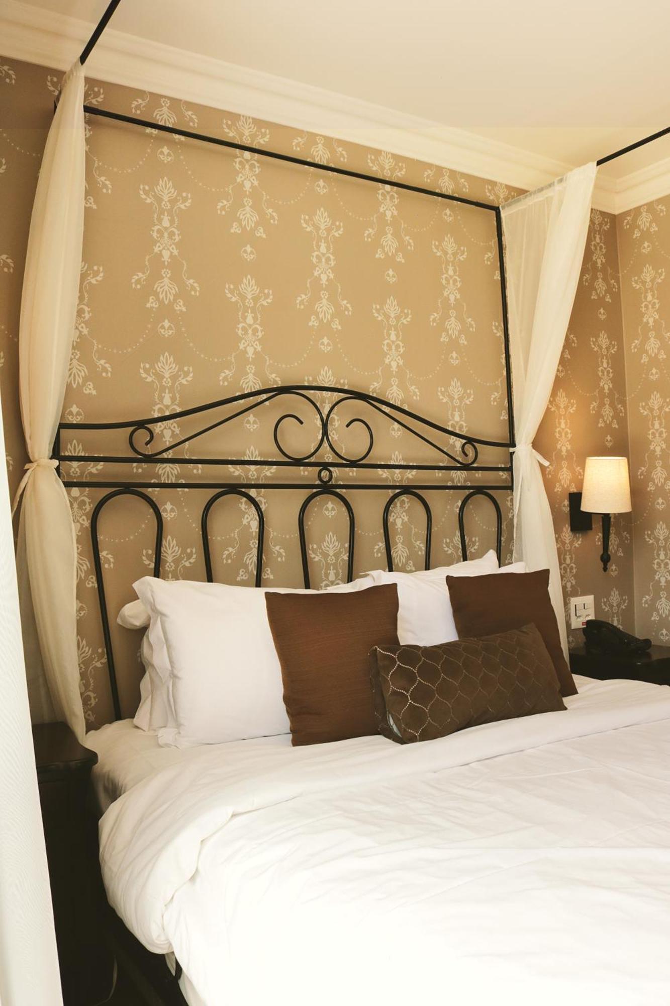 Buona Vitta Gramado Resort & Spa By Gramado Parks Buitenkant foto The photo shows a cozy bedroom setup featuring a decorative metal bed frame with a scroll design as the headboard. The bed is adorned with several white pillows and two brown decorative cushions. The wall behind the bed is covered with a light-colore