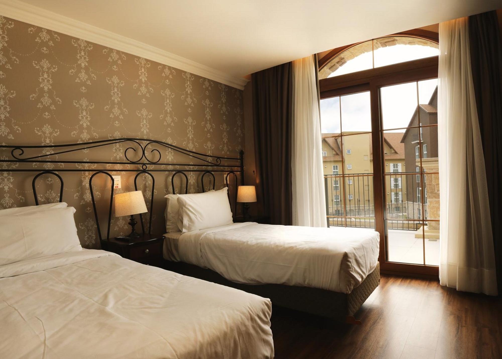 Buona Vitta Gramado Resort & Spa By Gramado Parks Buitenkant foto The photo shows a well-decorated hotel room featuring two beds. One bed is larger, likely a double bed, while the other is a single bed. The walls are adorned with a floral pattern, and there are bedside lamps next to the larger bed. Large windows wi