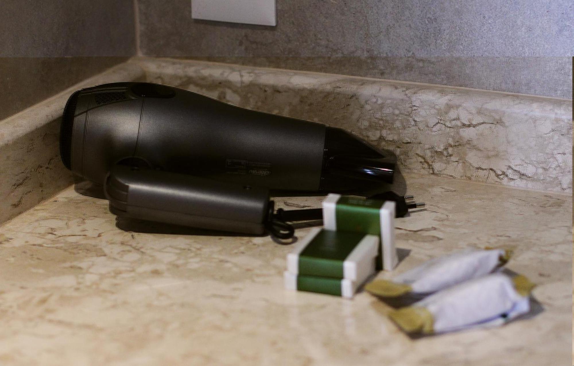 Buona Vitta Gramado Resort & Spa By Gramado Parks Buitenkant foto The photo shows a black hairdryer placed on a marble countertop. Next to the hairdryer, there are two wrapped items, likely toiletries, with green and white packaging. Additionally, there are two more items, also wrapped, which appear to be in simila