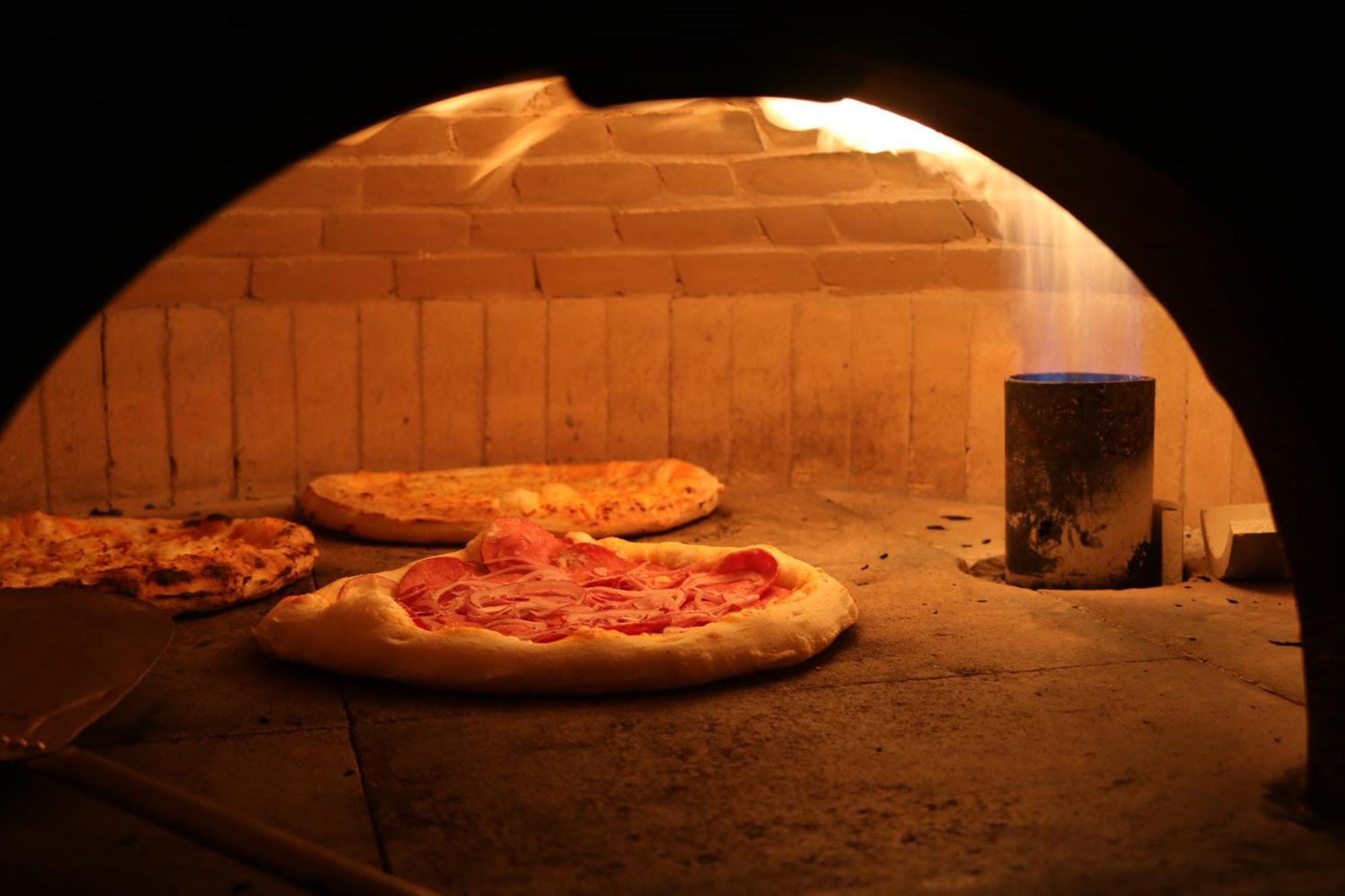 Buona Vitta Gramado Resort & Spa By Gramado Parks Buitenkant foto The photo shows a traditional pizza oven. Inside the oven, there are several pizzas placed on the stone surface. The pizzas appear to have various toppings, including what looks like cheese and possibly pepperoni. The oven has a warm, glowing ambianc